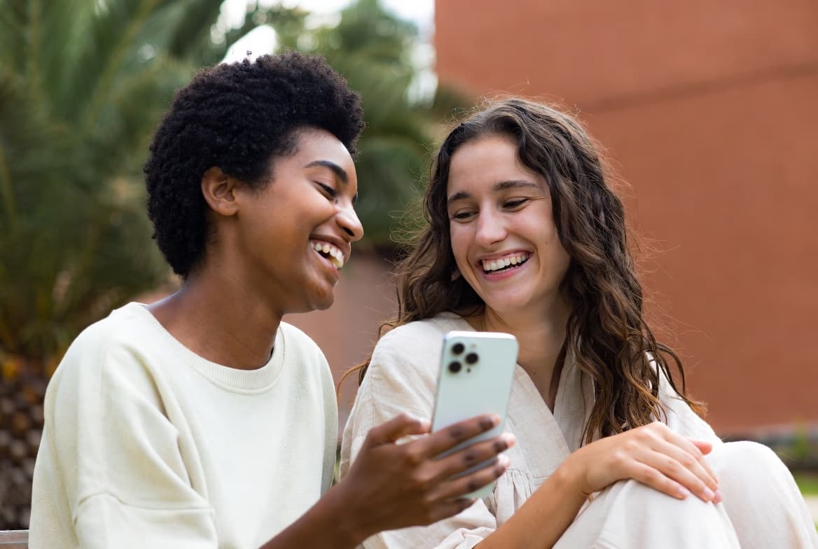 Two friends laughing together while one shows the other something on her phone